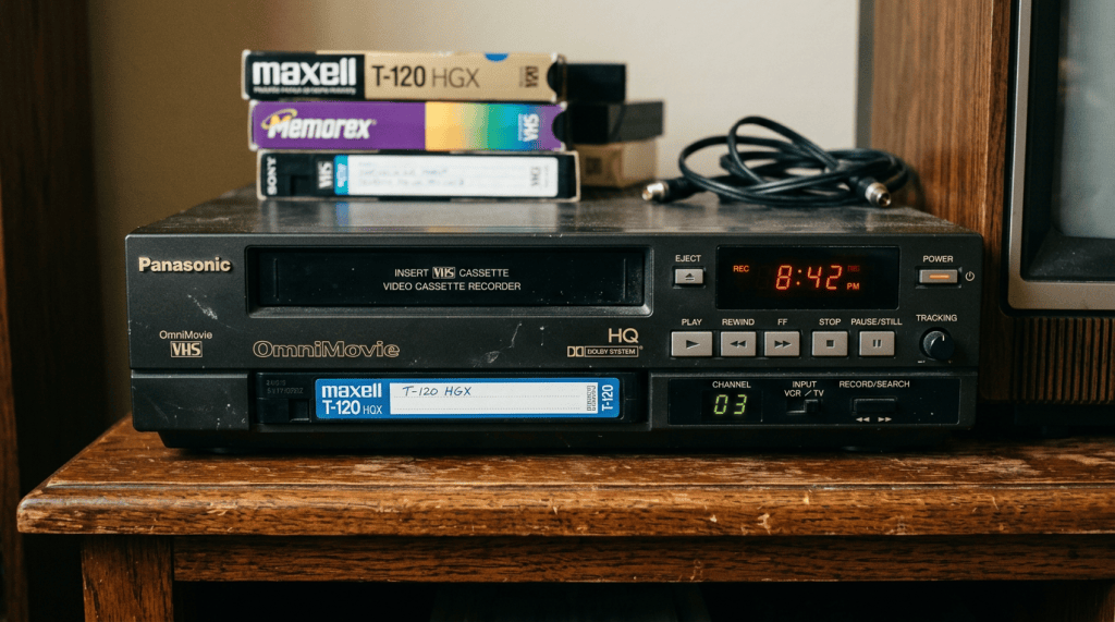 Panasonic OmniMovie VHS cassette player with Maxell T-120 tape loaded and three VHS tapes stacked on top